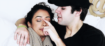 A Man Is Touching A Woman 'S Nose While Laying On A Bed GIF