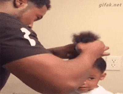 A Man Is Tying A Baby 'S Hair In A Ponytail . GIF