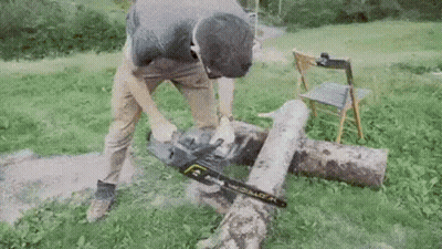 A Man Is Using A Chainsaw To Cut A Log . GIF