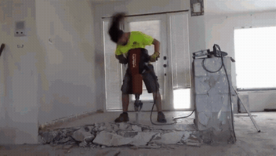 A Man Is Using A Hammer To Break A Wall In A Living Room . GIF