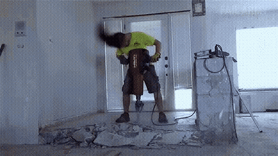 A Man Is Using A Hilti Hammer To Break A Wall GIF