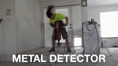 A Man Is Using A Metal Detector To Drill A Hole In A Wall GIF