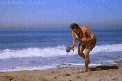 A Man Is Using A Metal Detector To Search For Something On The Beach . GIF