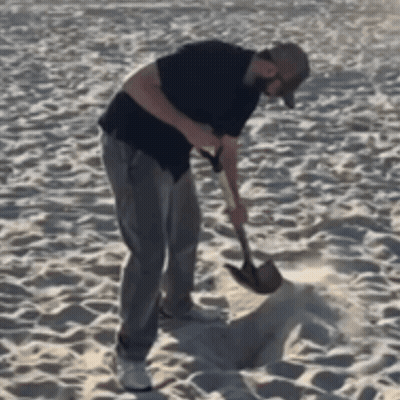 A Man Is Using A Shovel To Dig In The Sand GIF