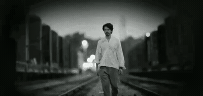 A Man Is Walking Along Train Tracks In A Black And White Photo . GIF