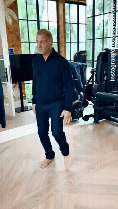 A Man Is Walking Barefoot In A Gym With A Tv On The Wall . GIF