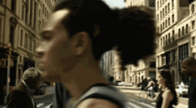 A Man Is Walking Down A City Street With A Woman In The Background . GIF
