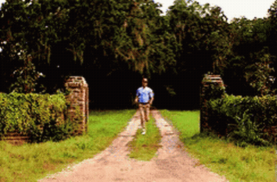 A Man Is Walking Down A Dirt Road In A Field GIF