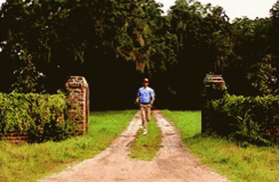 A Man Is Walking Down A Dirt Road In A Field GIF