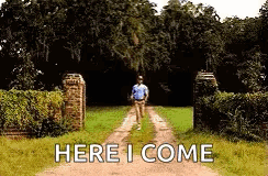 A Man Is Walking Down A Dirt Road With The Words `` Here I Come '' Written On The Ground . GIF