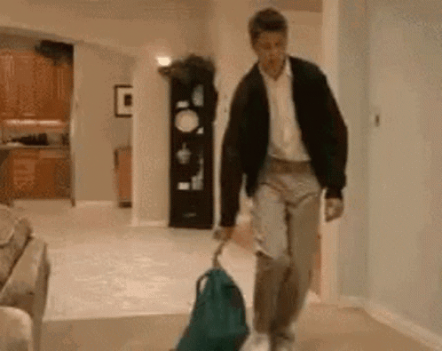 A Man Is Walking Down A Hallway Carrying A Backpack . GIF