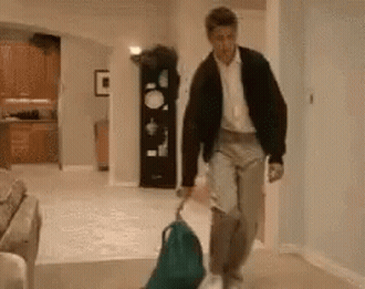 A Man Is Walking Down A Hallway With A Backpack And A Suitcase . GIF