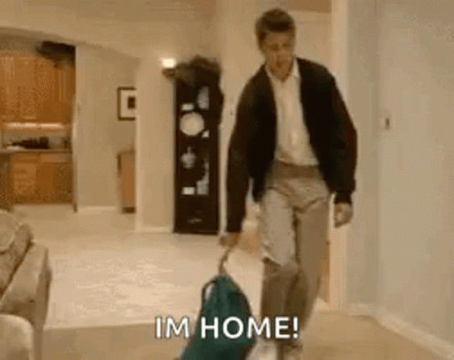 A Man Is Walking Down A Hallway With A Suitcase And A Dog And Says I 'M Home . GIF