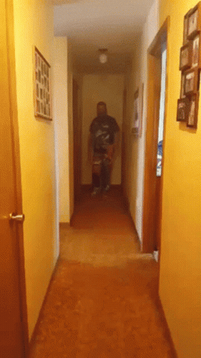 A Man Is Walking Down A Hallway With Pictures On The Walls GIF
