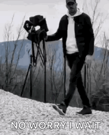 A Man Is Walking Down A Hill With A Camera In His Hand And Says `` No Worry I Wait '' . GIF