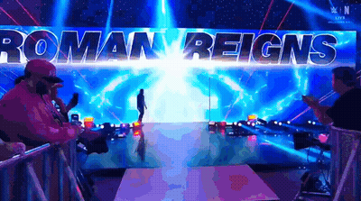 A Man Is Walking Down A Ramp With Roman Reigns Written On The Wall Behind Him GIF