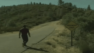 A Man Is Walking Down A Road Next To A Sign That Says Pavement Ends GIF