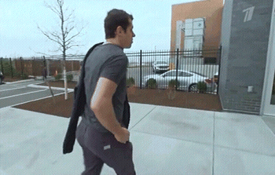 A Man Is Walking Down A Sidewalk In Front Of A Building With A Car Parked In Front Of It . GIF