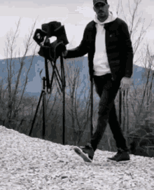 A Man Is Walking Down A Snowy Hill With A Camera . GIF