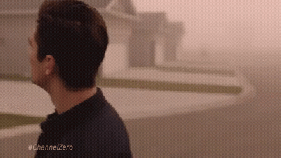 A Man Is Walking Down A Street In Front Of A House In The Fog . GIF