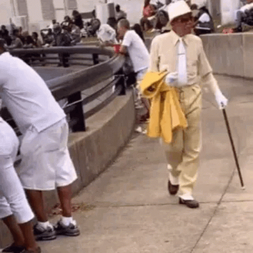 A Man Is Walking Down The Sidewalk With A Cane . GIF