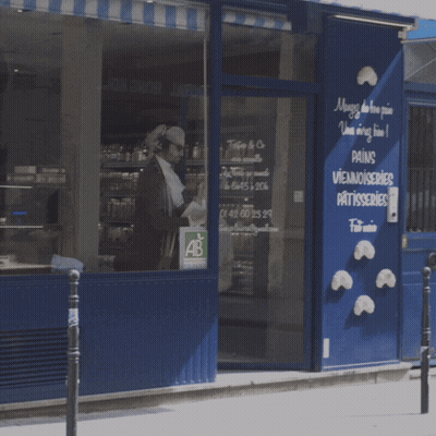 A Man Is Walking In Front Of A Store That Sells Pains Viennoiseries Patisseries GIF