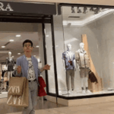 A Man Is Walking In Front Of A Store With A Bag That Says Zvra GIF
