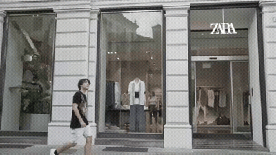 A Man Is Walking In Front Of A Store With A Mannequin In The Window . GIF