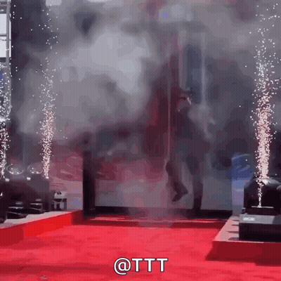 A Man Is Walking On A Red Carpet With Smoke Coming Out Of The Door GIF
