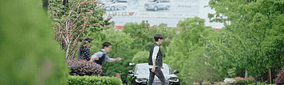 A Man Is Walking Past A Car In A Park . GIF