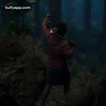 A Man Is Walking Through A Dark Forest With A Lantern . GIF