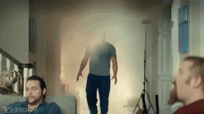 A Man Is Walking Through A Doorway With Smoke Coming Out Of It While A Man Sits On A Couch . GIF