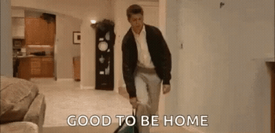 A Man Is Walking Through A Living Room Carrying A Suitcase And A Vacuum Cleaner . GIF