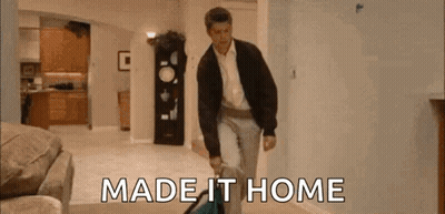 A Man Is Walking Through A Living Room Carrying A Suitcase And The Words `` Made It Home '' . GIF