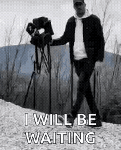 A Man Is Walking With A Camera On A Tripod While Holding A Camera . GIF