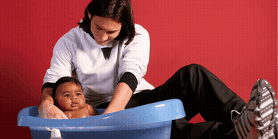 A Man Is Washing A Baby In A Blue Bathtub GIF