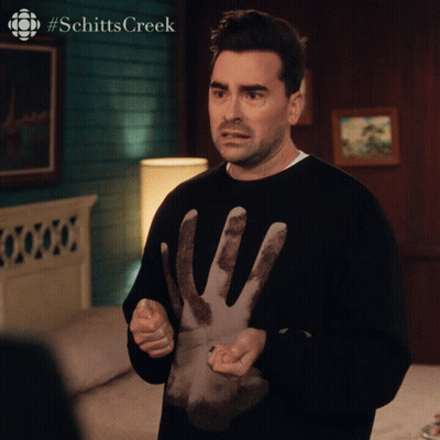 A Man Is Wearing A Black Sweater With A Hand On It And The Words Schitts Creek On The Bottom GIF