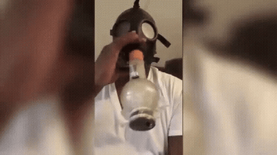A Man Is Wearing A Gas Mask And Smoking A Bong . GIF