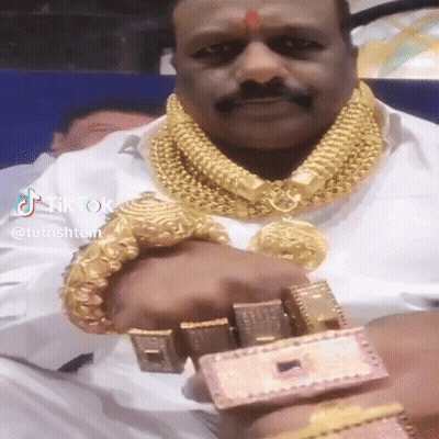 A Man Is Wearing A Lot Of Gold Jewelry Including A Gold Necklace And Bracelets . GIF
