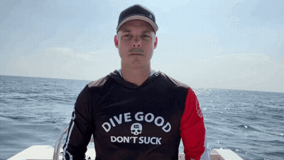 A Man Is Wearing A Shirt That Says Dive Good Don 'T Suck GIF