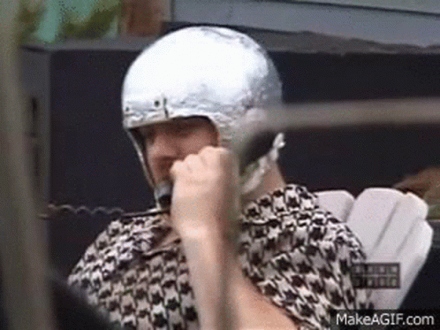 A Man Is Wearing A Silver Helmet And Talking On A Cell Phone . GIF