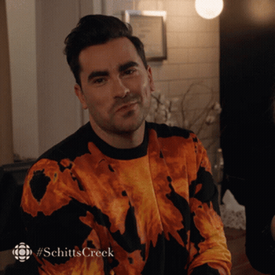 A Man Is Wearing A Sweater That Says Schitts Creek On The Bottom GIF