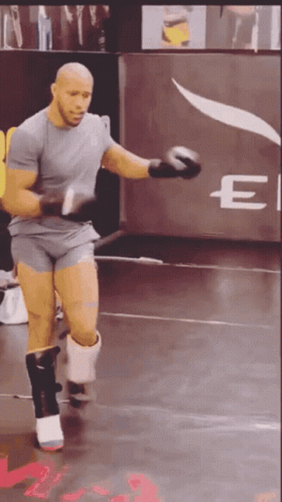 A Man Is Wearing Boxing Gloves In Front Of A Sign That Says E GIF