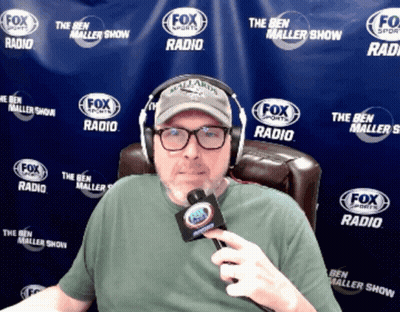 A Man Is Wearing Headphones And Holding A Microphone In Front Of A Fox Sports Radio Banner GIF