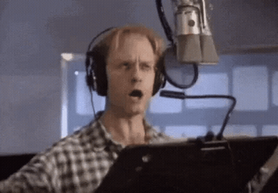 A Man Is Wearing Headphones And Singing Into A Microphone . GIF