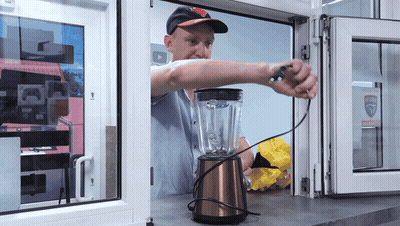 A Man Is Working On A Blender In Front Of A Window That Has A Sticker That Says ' Safety ' GIF