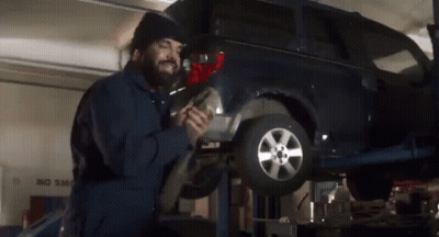 A Man Is Working On A Car In A Garage With A No Smog Sign In The Background GIF