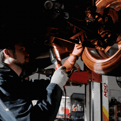 A Man Is Working Under A Car In A Garage With A Msd Lift In The Background GIF