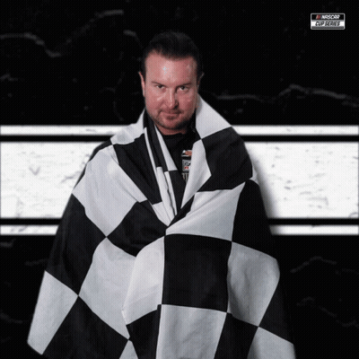 A Man Is Wrapped In A Black And White Checkered Flag With A Nascar Logo In The Background GIF