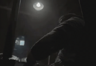 A Man Is Wrapped In Duct Tape And Sitting In A Chair In A Dark Room . GIF